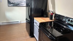 A kitchen with a black refrigerator, a wooden countertop, a stove, and hanging pots.