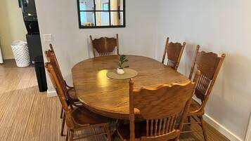 Een eetgedeelte met een ronde houten tafel, zes stoelen, een kleine potplant en een zwart apparaat.