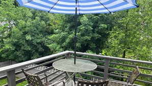 A deck with a round table and two chairs, surrounded by a wooden railing, overlooking a lush green landscape.