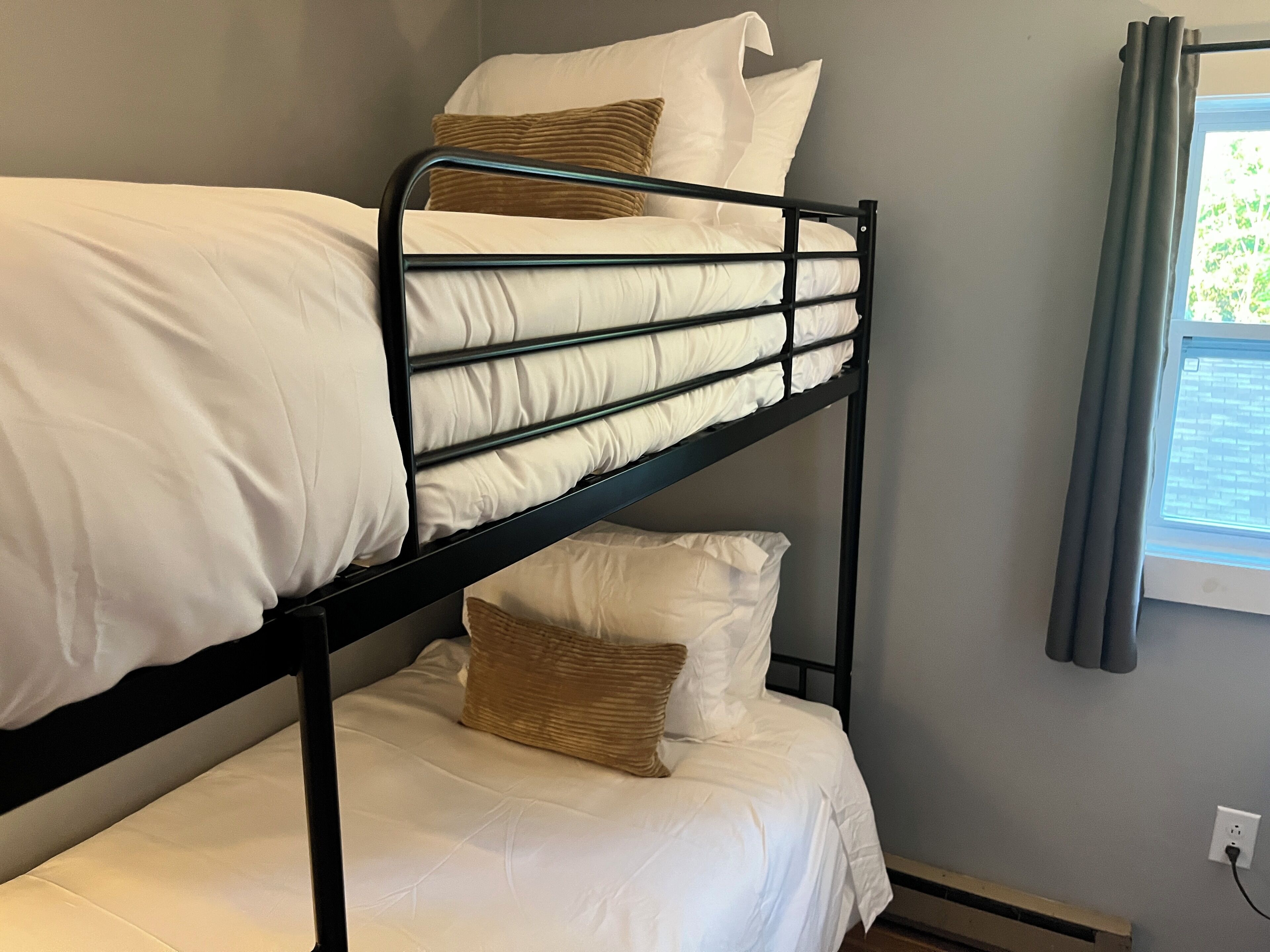 A bunk bed with white bedding and a window with curtains.
