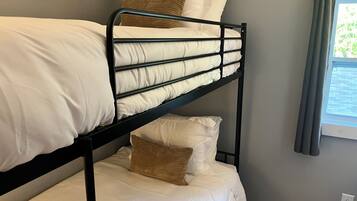 A bunk bed with white bedding and a window with curtains.