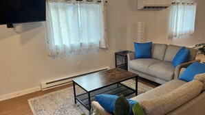 A living room with a sofa, a coffee table, a TV, and an air conditioner.