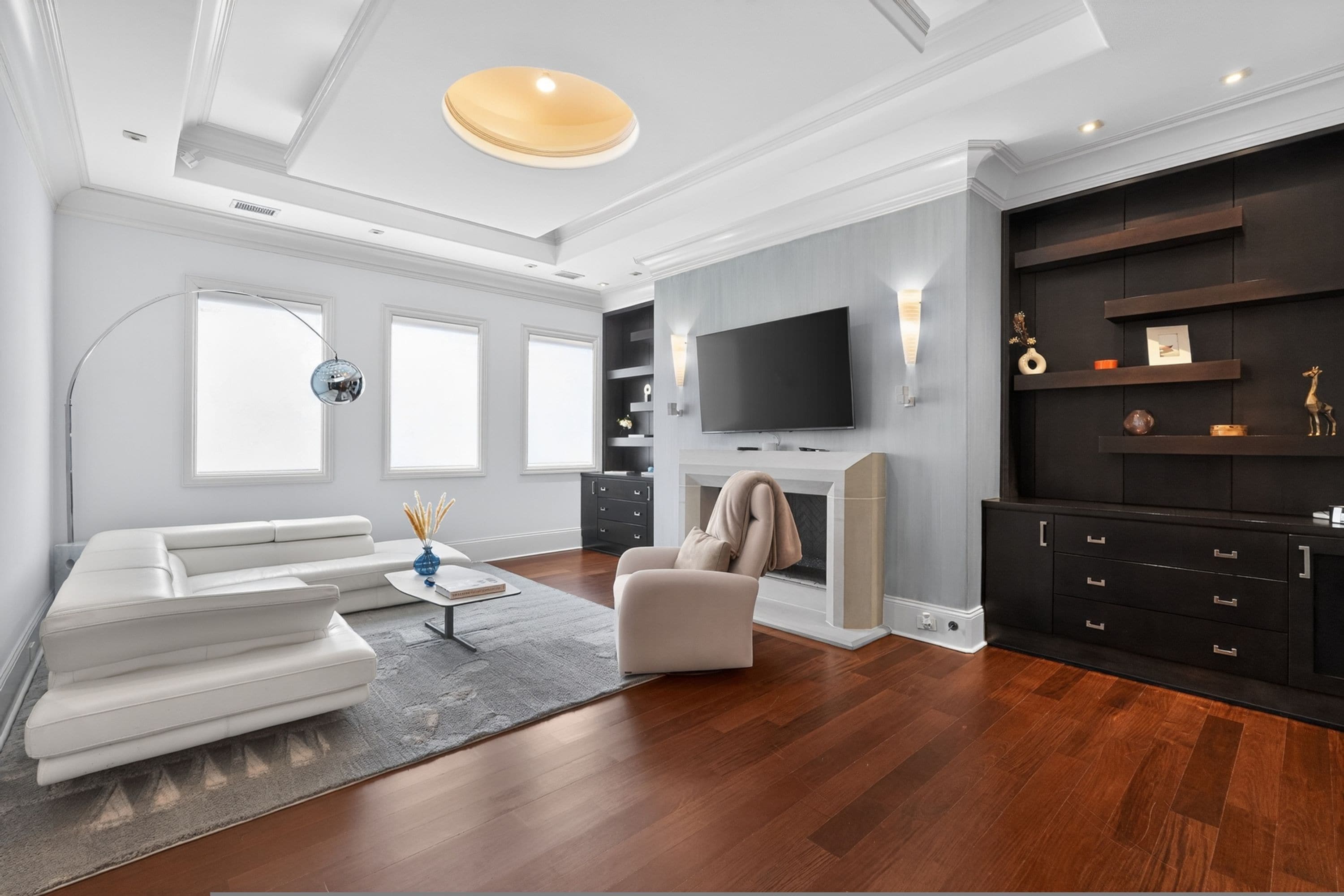A modern living room with a white sectional sofa, a beige armchair, a flat-screen TV mounted on a dark wall, a fireplace, and a built-in black entertainment unit.