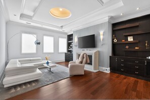 A modern living room with a white sectional sofa, a beige armchair, a flat-screen TV mounted on a dark wall, a fireplace, and a built-in black entertainment unit. - Marietta Mansion in Marietta (Marietta)