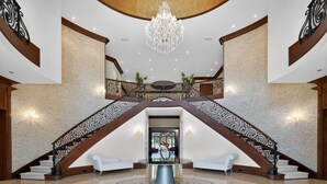 A grand lobby with a high ceiling, a chandelier, a grand staircase with ornate railings, and a central round table. - Marietta Mansion in Marietta (Marietta)