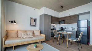 Un'area living moderna con un divano, un tavolo da pranzo, sedie, un piccolo tavolino rotondo, una lampada e una cucina sullo sfondo.