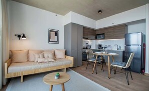 Un espacio moderno para estar con un sofá, una mesa de comedor, sillas, una pequeña mesa redonda, una lámpara y una cocina al fondo.