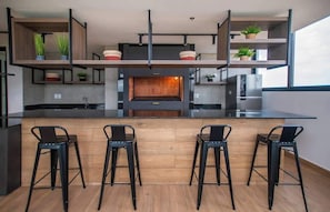 Una cocina moderna con una isla central, taburetes de bar y estanterías empotradas con plantas.