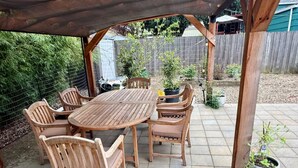 Een terras buiten met een houten tafel en stoelen, omgeven door een houten pergola.