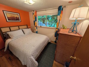 A bedroom with a bed, a window with curtains, a lamp, a dresser, and a framed picture on the wall.