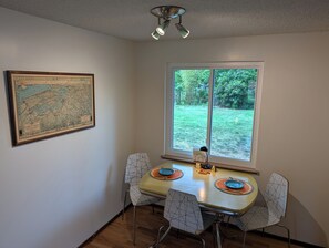 A dining area with a table, chairs, a map, and a window with a view of greenery.