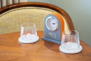 Una mesa de madera con dos vasos transparentes y un reloj sobre un soporte.