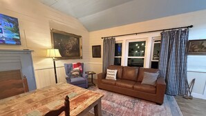 A cozy living room with a wooden table, a brown leather sofa, a blue armchair, and a checkered curtain.