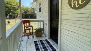 A porch with a wooden chair, a potted plant, a welcome mat, and a door with a 'hi' sign.