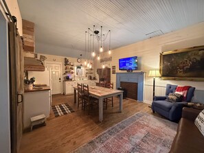 A cozy living room with a fireplace, a television, and a dining area with wooden furniture. - Cozy Cottage near Lake Fork! (Yantis)
