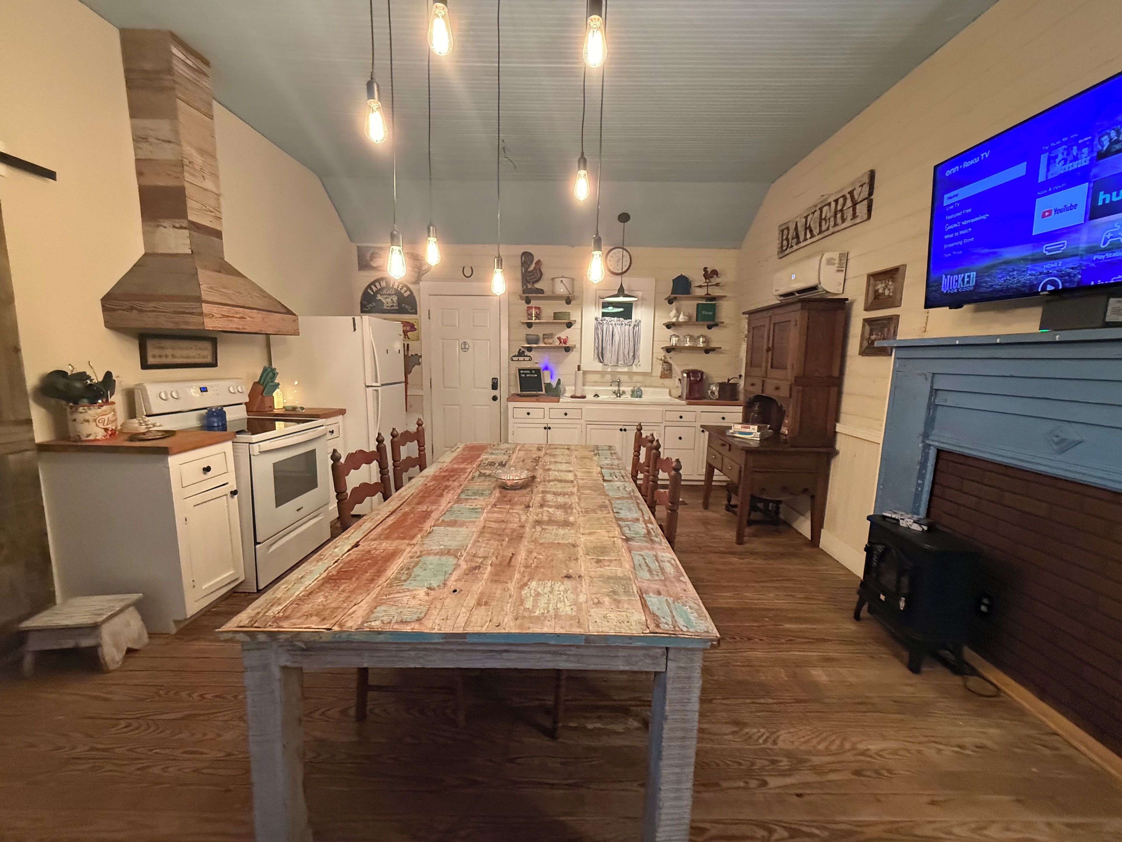 A kitchen with a dining table, wooden cabinets, a stove, and a TV mounted on the wall.