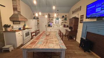 A kitchen with a dining table, wooden cabinets, a stove, and a TV mounted on the wall.