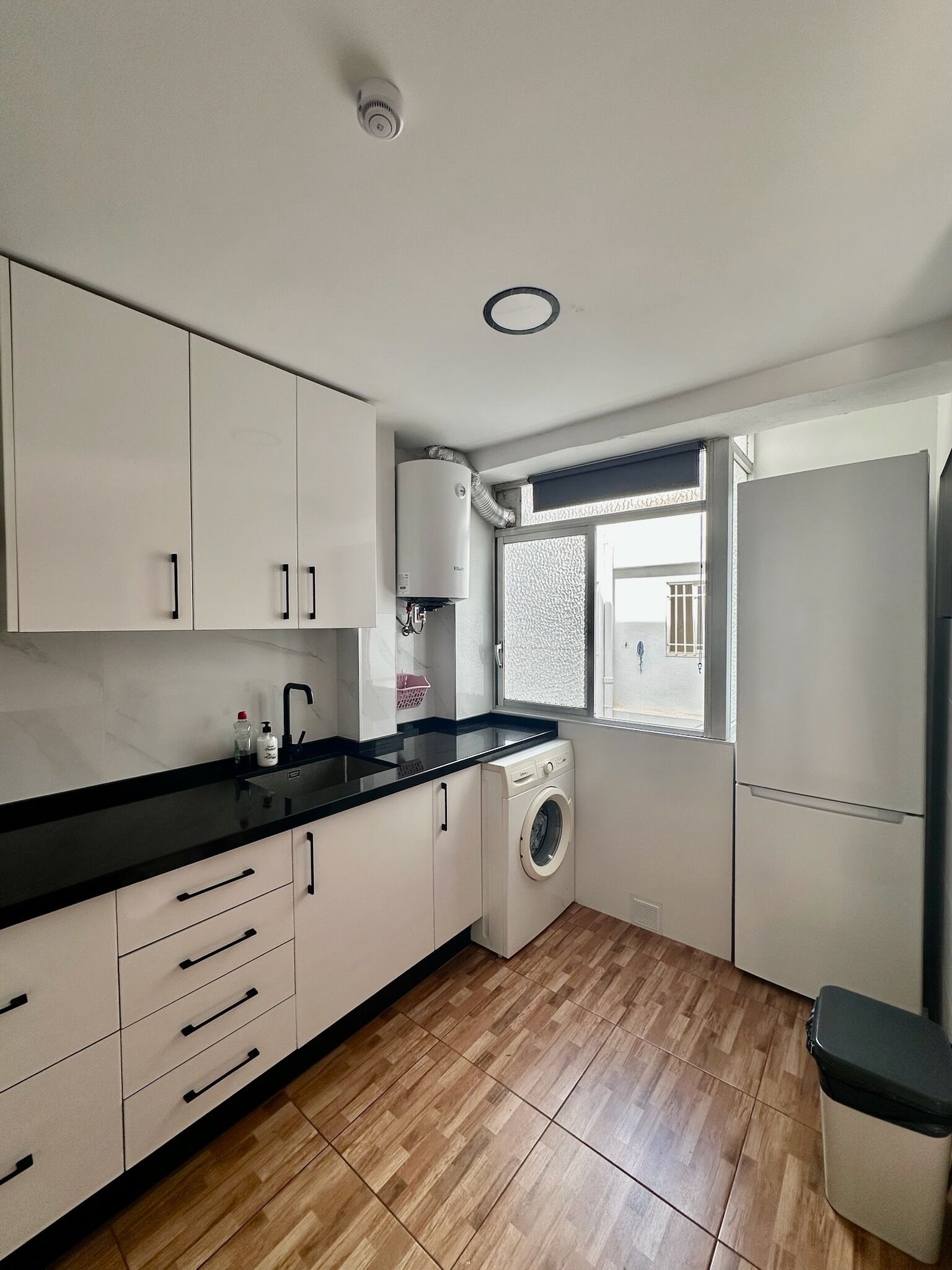 A modern kitchen with white cabinets, a black countertop, a washing machine, and a refrigerator.