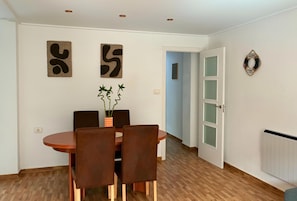 Uma área de refeições com uma mesa redonda e quatro cadeiras, um vaso com plantas e arte abstrata na parede.