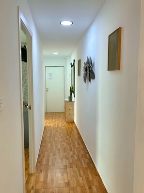 Ein Flur mit Holzdielen, weißen Wänden und einer Tür am Ende.