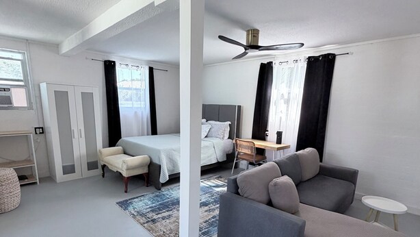 A modern hotel room with a bed, a sofa, a desk, and a ceiling fan. - Your Cozy Private Studio by the Beach (Ormond Beach)