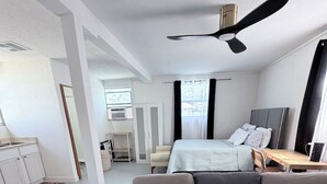 A modern, well-lit bedroom with a large bed, a sofa, a desk, and a ceiling fan. - Your Cozy Private Studio by the Beach (Ormond Beach)