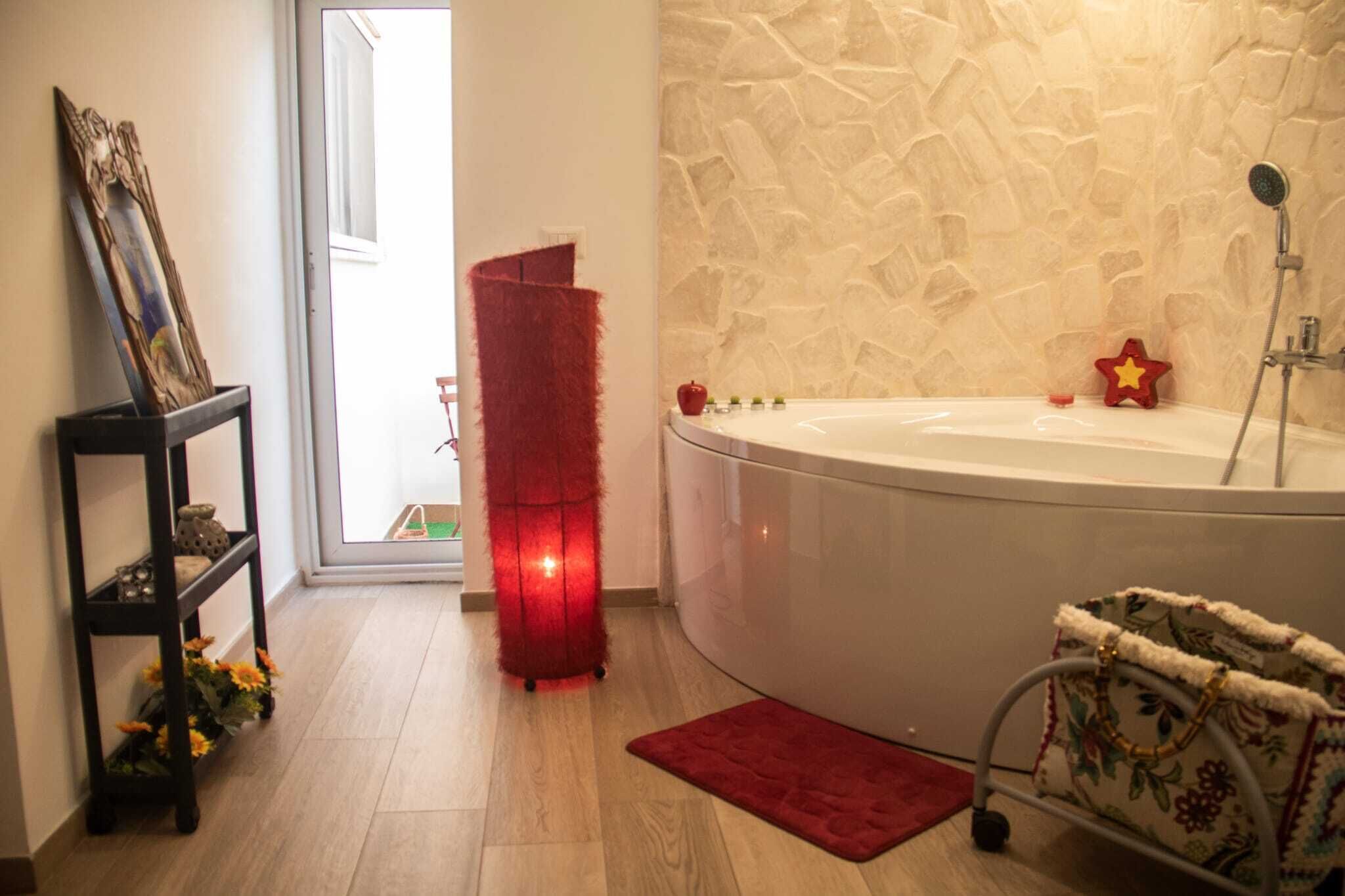 Une salle de bain avec une baignoire, un tabouret rouge et moelleux, une décoration en forme d’étoile rouge, une petite table avec un cadre photo et un tapis rouge.