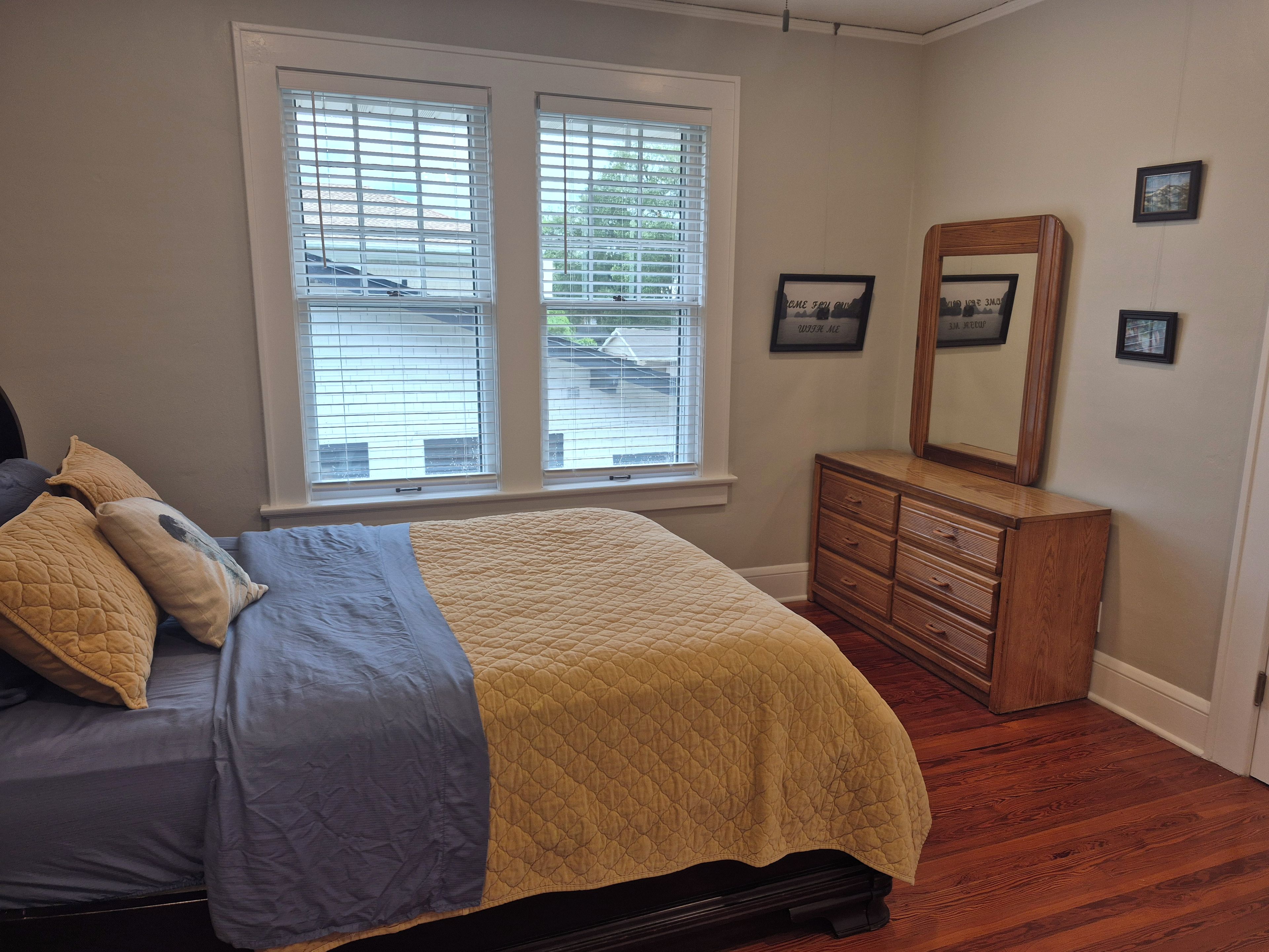 Ein Schlafzimmer mit Bett, Schminktisch, Fenster mit Jalousien und Spiegel an der Wand.