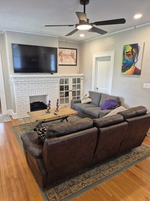 A living room with a fireplace, a ceiling fan, a flat-screen TV, and a sofa. - Le Magnolia Magnifique: a 3-bedroom townhome in historic Riverside (Jacksonville)