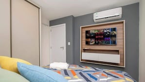 Ein Schlafzimmer mit Bett, Kissen, einem an der Wand montierten Fernseher und einer Klimaanlage.