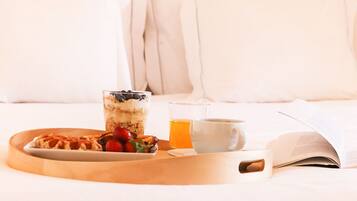 A breakfast tray on a bed with waffles, berries, a glass of juice, a cup, and an open book.
