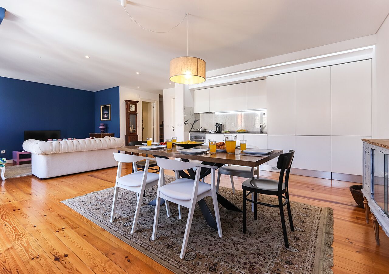 A modern kitchen with white cabinets, a dining table with chairs, and a blue accent wall.