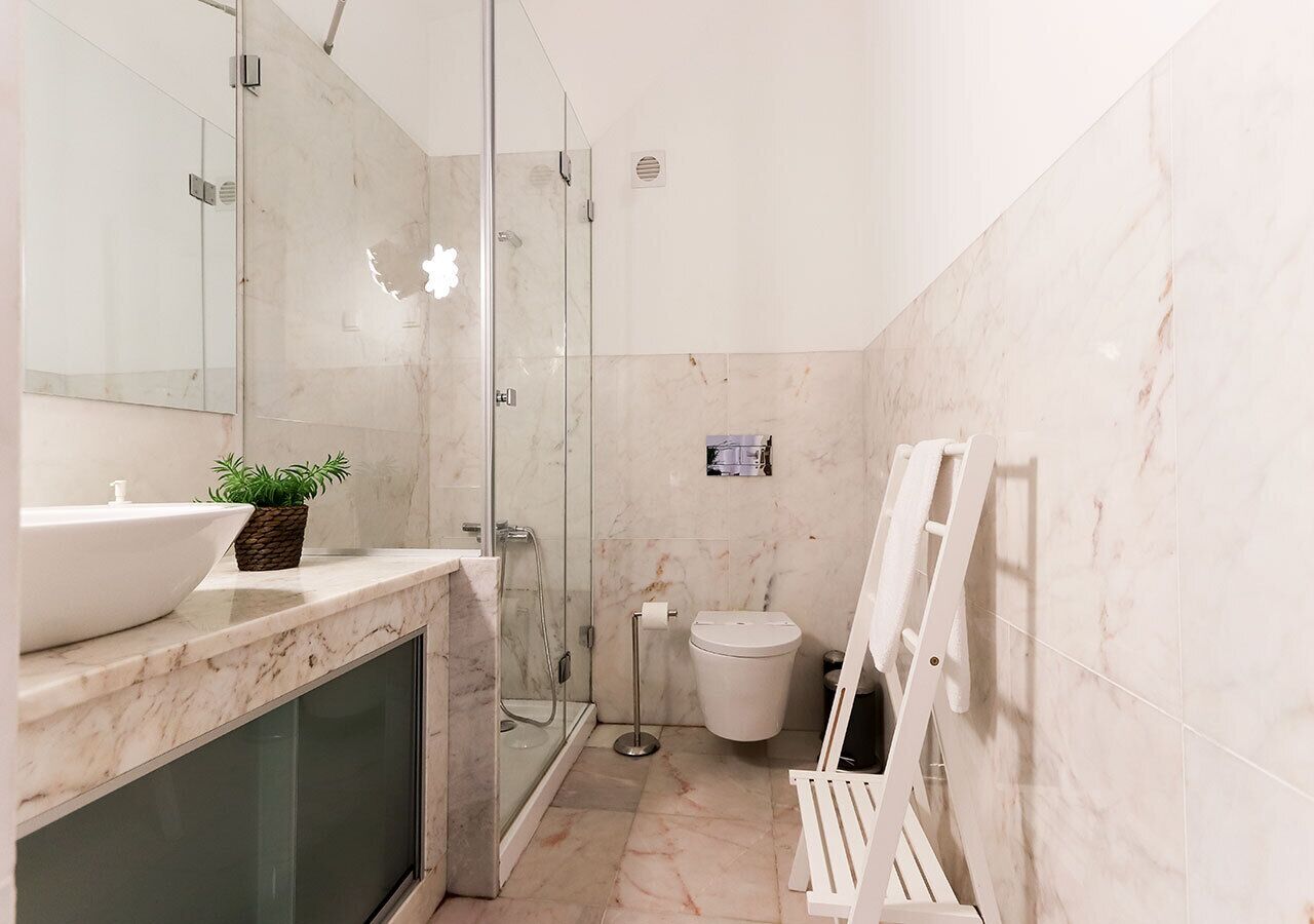 A bathroom with a glass shower enclosure, a toilet, a sink with a marble countertop, and a mirror.