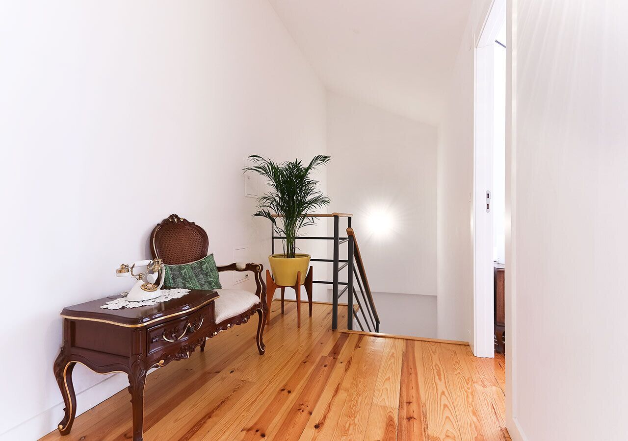 Ein Zimmer mit Holzboden, einem Schreibtisch mit Telefon, einem Stuhl, einer Pflanze und einer Treppe.