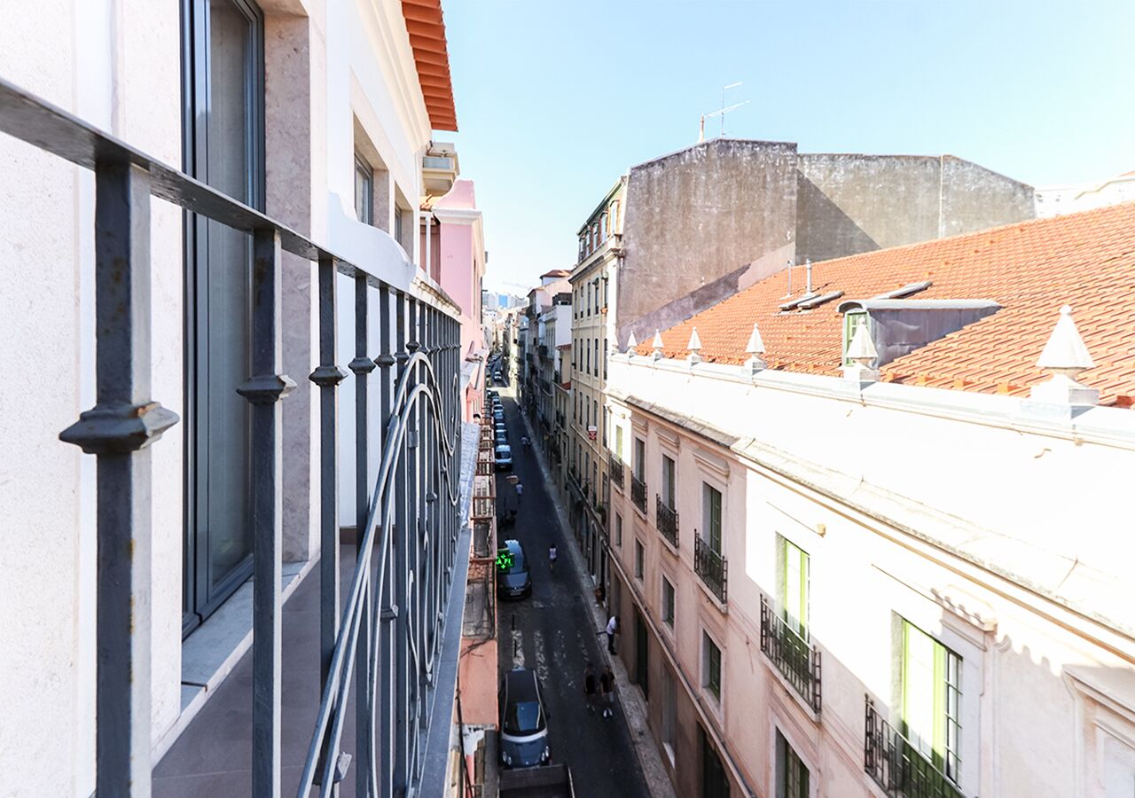 A narrow street with buildings on either side, a clear sky, and a distant view of a fort-like structure.