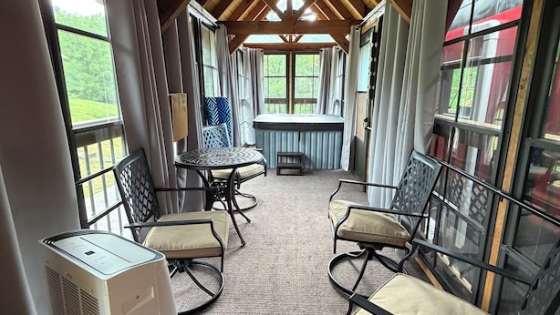 A covered outdoor seating area with a table and chairs, a radiator, and large windows.