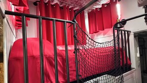 A bunk bed with a net barrier, red curtains, and a patterned ceiling.