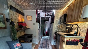 A narrow hallway with a wooden floor, a sofa, a lamp, and a kitchen area with cabinets and a sink.