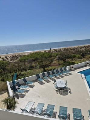 A poolside area with lounge chairs and a table, overlooking a beach and ocean. - Pyramid 2D Oceanfront with Heated Pool (Ocean City)
