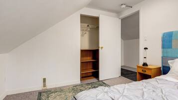 A bedroom with a bed, a nightstand, a lamp, a wardrobe, and a door leading to another room.