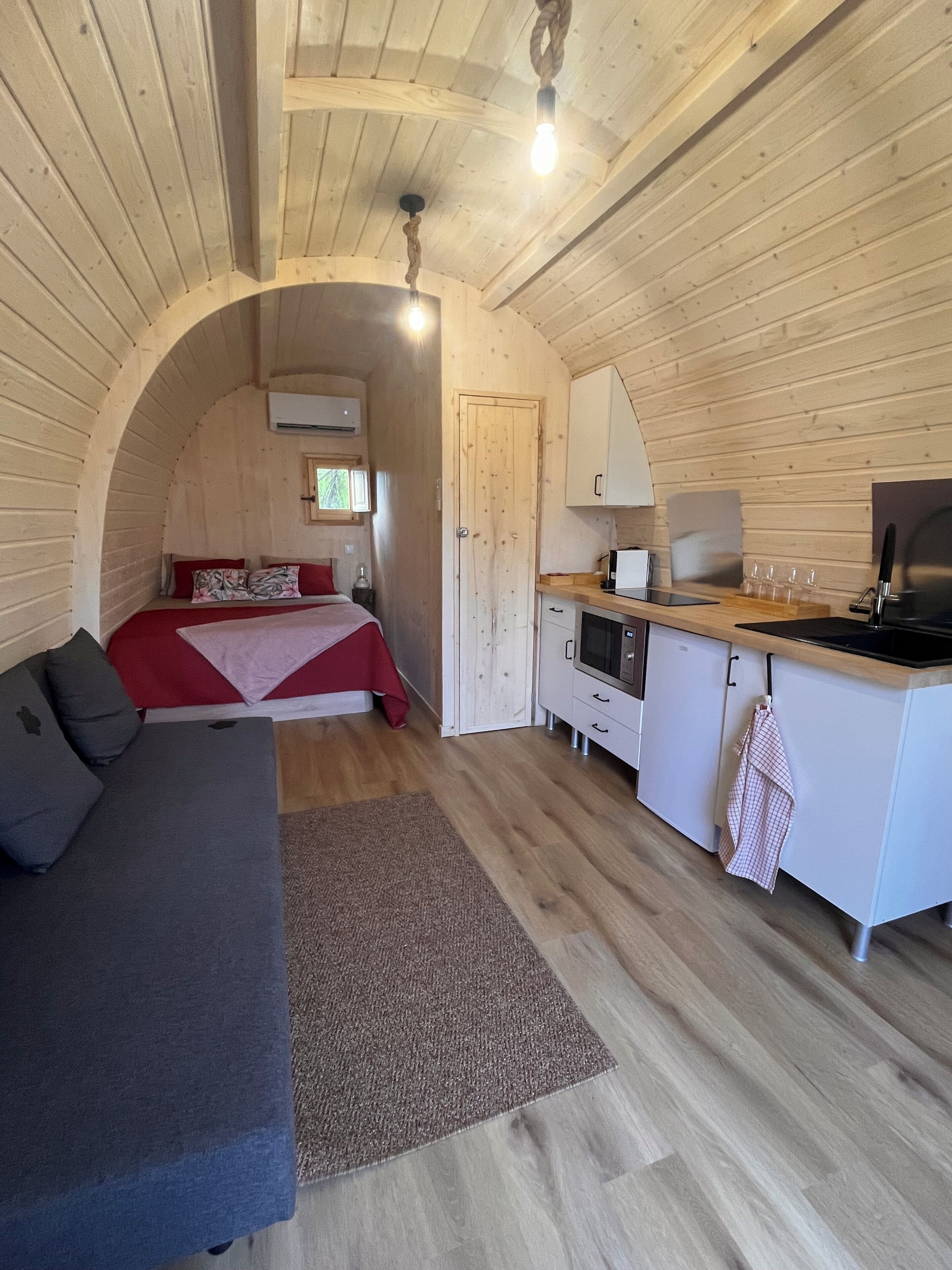 A cozy, compact room with a bed, a sofa, a kitchenette, and a wooden ceiling.
