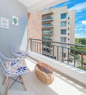 Ein Balkon mit zwei Stühlen, einem kleinen Tisch und einem Korbsitzhocker.