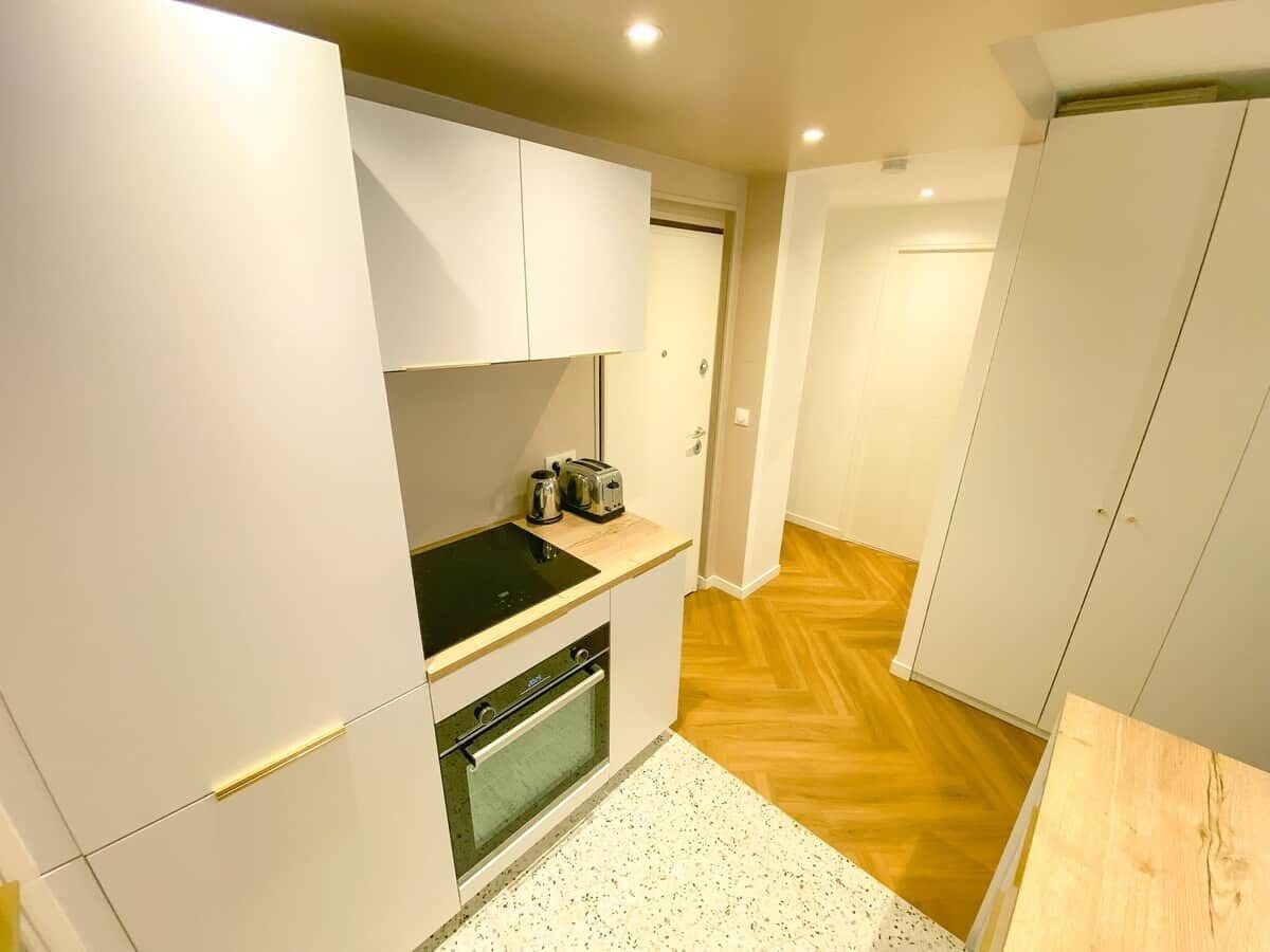 Une cuisine de taille réduite avec des meubles blancs, une cuisinière noire et un plancher en bois.