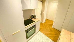 Pieni, käytännöllinen keittiö, jossa on valkoiset kaapit, musta liesi ja puulattia.