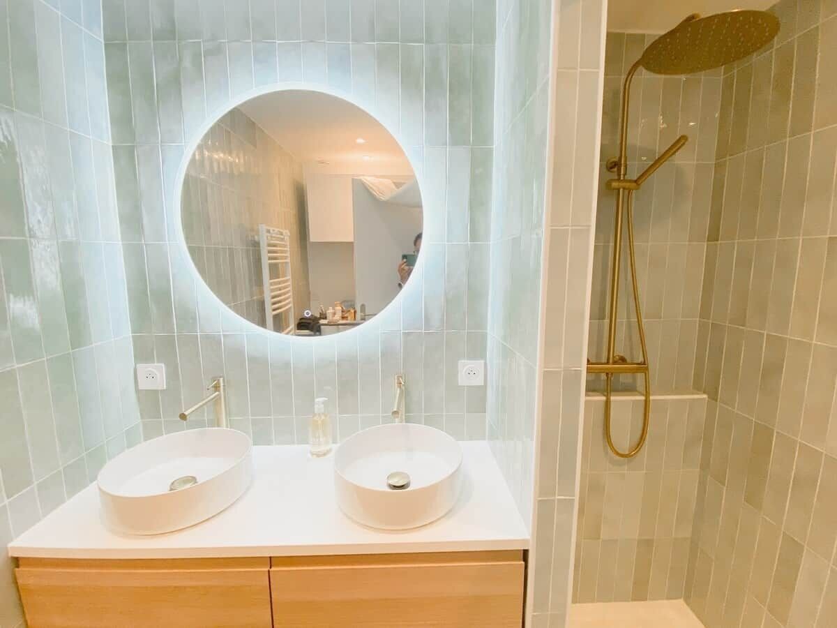 Une salle de bain avec deux lavabos, un miroir rond et une douche.