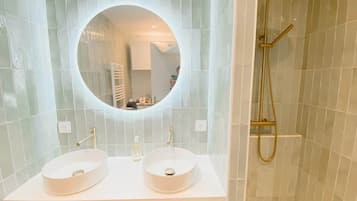 Une salle de bain avec deux lavabos, un miroir rond et une douche.