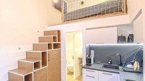 Cocina moderna con horno empotrado, un lavamanos y una cafetera. Se ve una escalera de madera que sube a un segundo piso.