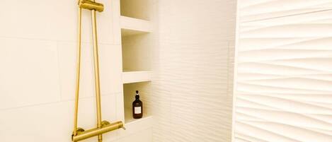 A shower with a gold showerhead and a bottle of shampoo on a shelf.