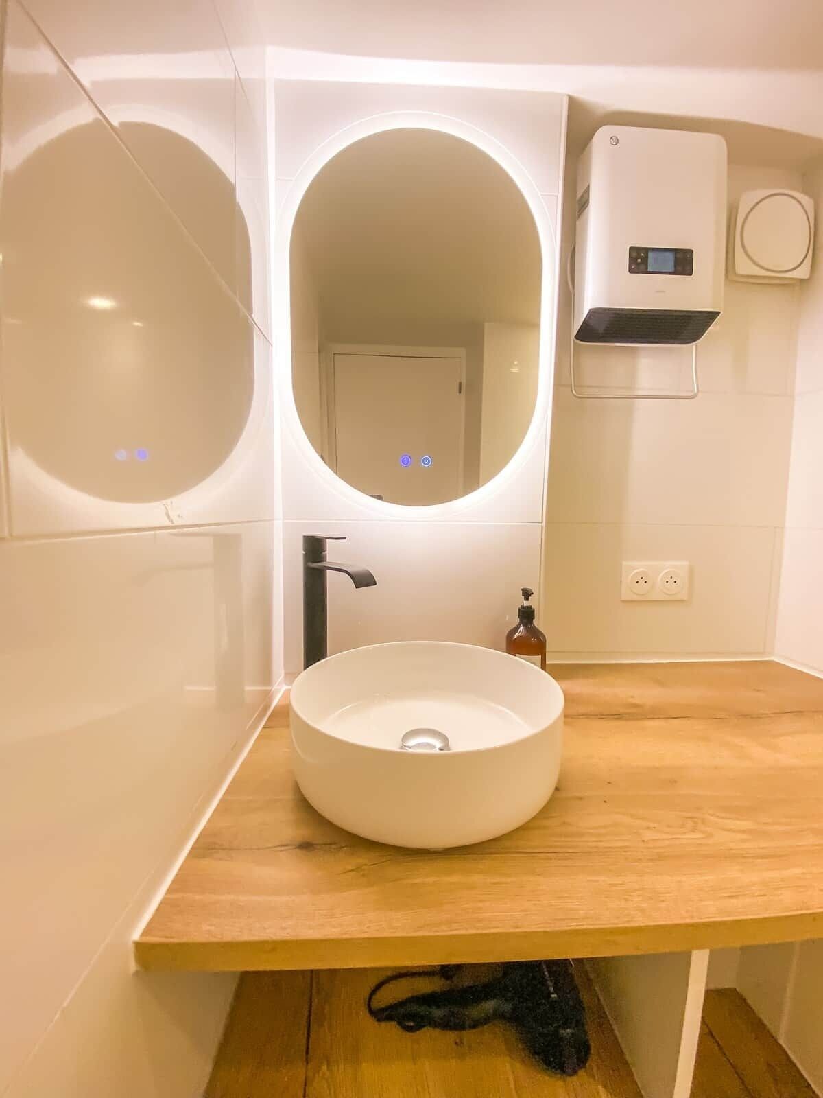 Un baño moderno con un lavabo redondo, un espejo grande y un calentador instalado en la pared.