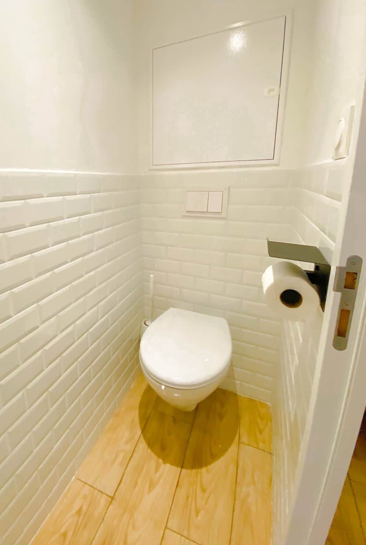 Ein kleines Badezimmer mit weißen Wänden, einer Toilette, einem Holzboden und einer weißen Tür mit Griff.